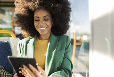 Smiling businesswoman using tablet PC in tram - JCCMF05284