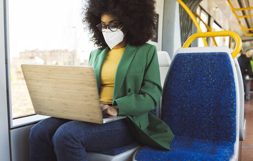 Pendler mit Gesichtsschutzmaske bei der Arbeit mit einem Laptop in der Straßenbahn - JCCMF05287