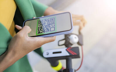 Pendler scannt QR-Code mit seinem Smartphone auf einem Elektroroller - JCCMF05304