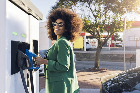 Happy businesswoman with fuel pump at gas station - JCCMF05310