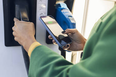 Commuter scanning QR code on mobile phone at gas station - JCCMF05312