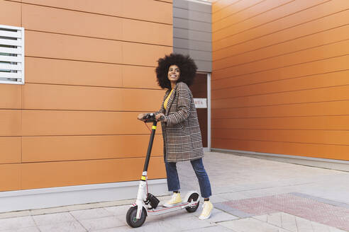 Woman with electric push scooter standing on footpath - JCCMF05333