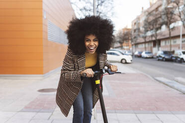 Cheerful woman riding electric push scooter on footpath - JCCMF05334