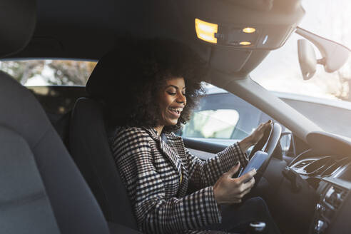 Fröhliche Frau benutzt Smartphone im Auto - JCCMF05343