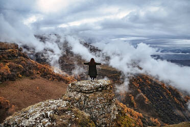 Female hiker standing with outstretched arms on top of outcrop in autumn mountains of North Caucasus - KNTF06656