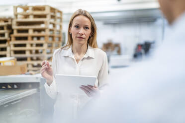 Blond businesswoman with tablet PC looking at colleague in industry - DIGF17549