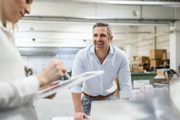 Happy businessman looking at businesswoman using tablet PC in industry - DIGF17551