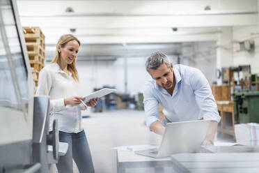 Blond businesswoman looking at businessman discussing over laptop in industry - DIGF17554