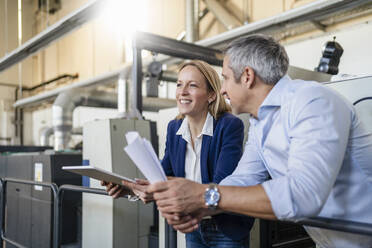 Smiling blond businesswoman with tablet PC standing by colleague in factory - DIGF17568