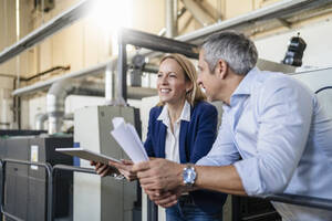 Lächelnde blonde Geschäftsfrau mit Tablet-PC, die neben einem Kollegen in einer Fabrik steht - DIGF17568