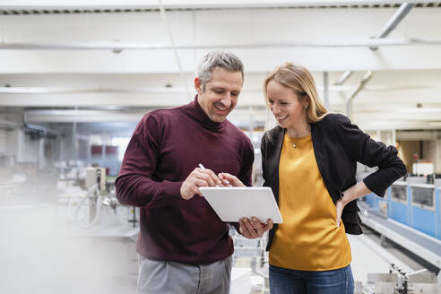 Glückliche Geschäftsfrau und Geschäftsmann teilen sich einen Tablet-PC in der Industrie - DIGF17571