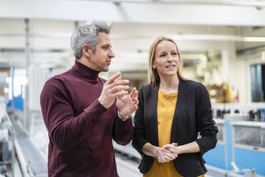 Businessman sharing ideas with blond businesswoman in industry - DIGF17574