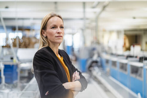 Thoughtful businesswoman standing with arms crossed in factory - DIGF17581