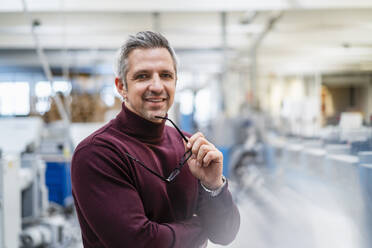 Smiling businessman with eyeglasses in factory - DIGF17587