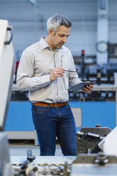 Businesswoman holding eyeglasses looking at tablet PC in industry - DIGF17600