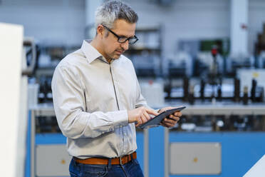 Businessman wearing eyeglasses using tablet PC in factory - DIGF17601