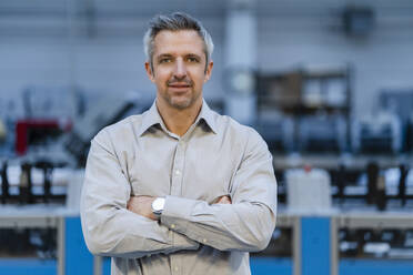 Businessman standing with arms crossed in factory - DIGF17602