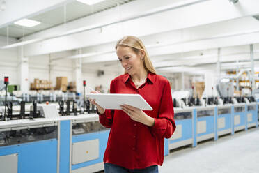 Lächelnde blonde Geschäftsfrau mit Tablet-PC bei der Arbeit in einer Fabrik - DIGF17608