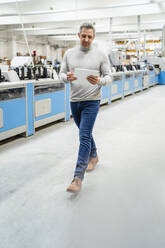 Businessman using tablet PC walking in production hall - DIGF17617