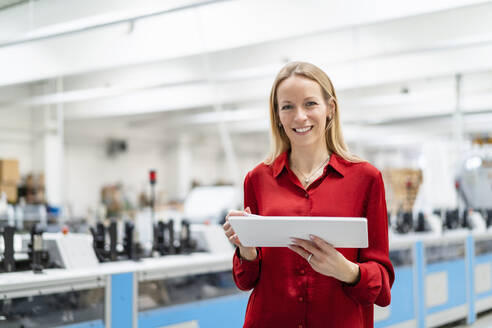 Happy businesswoman with tablet PC in factory - DIGF17624