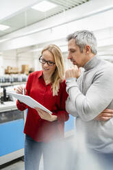 Geschäftsfrau mit Brille, die mit einem Kollegen in einer Fabrik über einen Tablet-PC diskutiert - DIGF17627