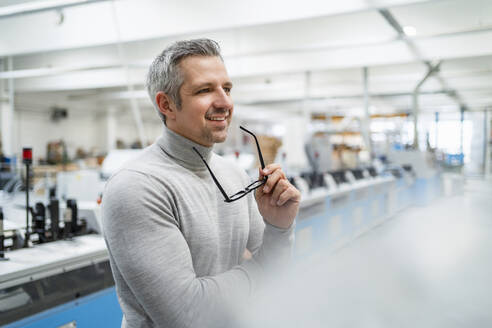 Lächelnder Geschäftsmann mit Brille in einer Fabrik - DIGF17633