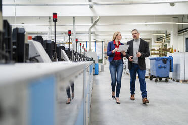 Businessman and businesswoman sharing ideas walking in production wall - DIGF17637