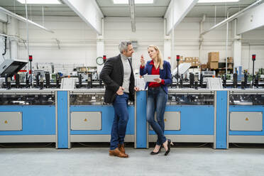 Businesswoman holding tablet PC discussing with businessman standing by machinery in factory - DIGF17639