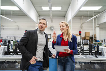 Smiling businesswoman holding tablet PC sharing ideas with colleague standing by machinery - DIGF17640