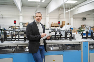 Geschäftsmann mit Tablet-PC an einer Maschine in einer Fabrik - DIGF17647