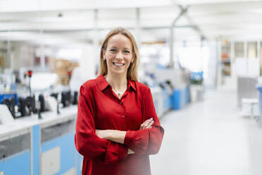 Happy blond businesswoman standing with arms crossed in factory - DIGF17648