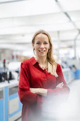 Smiling blond businesswoman standing with arms crossed in factory - DIGF17649