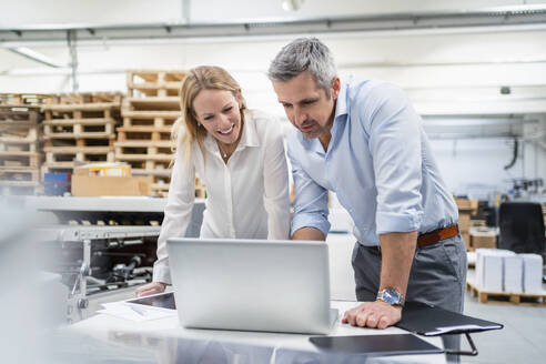 Geschäftsmann und Geschäftsfrau teilen sich einen Laptop am Schreibtisch in einer Fabrik - DIGF17657