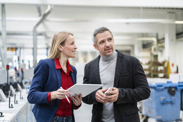 Businessman standing by businesswoman holding tablet PC in factory - DIGF17666