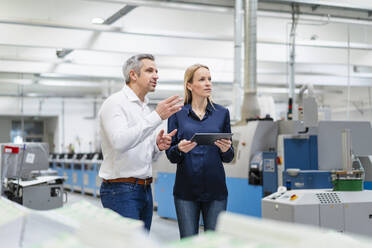 Businessman sharing ideas with businesswoman holding tablet PC in factory - DIGF17670