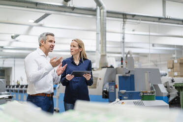 Blond businesswoman with tablet PC looking at colleague discussing in industry - DIGF17671