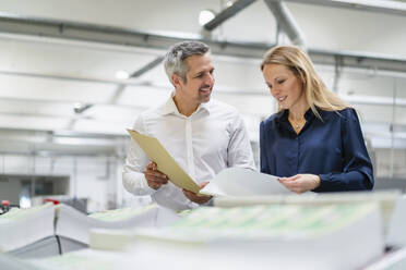 Smiling businessman discussing with colleague reading documents in factory - DIGF17676