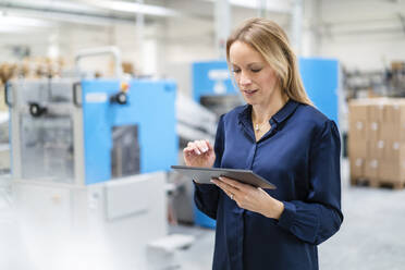 Blond businesswoman using tablet PC working in factory - DIGF17693