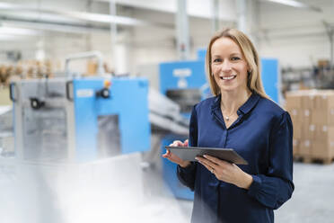 Glückliche Geschäftsfrau mit Tablet-PC in einer Fabrik stehend - DIGF17694