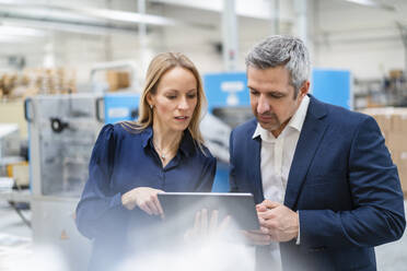 Blond businesswoman sharing tablet PC with colleague in factory - DIGF17701