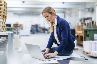 Geschäftsfrau mit Laptop auf dem Schreibtisch in einer Fabrik - DIGF17708