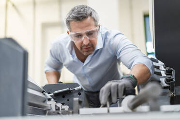 Geschäftsmann mit Schutzbrille bei der Überprüfung von Maschinen in einer Fabrik - DIGF17714