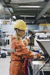 Young female industrial worker in uniform using manufacturing machinery at factory - MASF28245