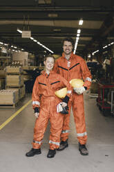 Porträt eines lächelnden männlichen und weiblichen Mitarbeiters in Uniform, die in einem Fabriklager stehen - MASF28251
