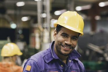 Porträt eines selbstbewussten männlichen Arbeiters mit Schutzhelm in einer Fabrik - MASF28254