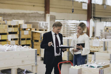 Businessman discussing with female manager in factory warehouse - MASF28257