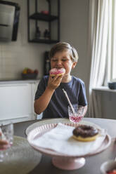 Junge isst Doughnut am Wohnzimmertisch - MASF28305