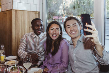 Fröhliche männliche und weibliche Freunde machen ein Selfie mit ihrem Smartphone im Restaurant - MASF28346