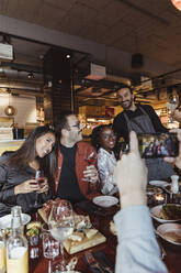 Ausgeschnittenes Bild eines Mannes, der mit seinem Smartphone in einem Restaurant ein Foto von männlichen und weiblichen Freunden macht - MASF28348