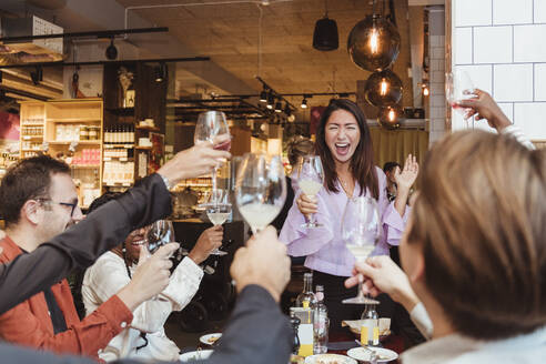 Fröhliche männliche und weibliche Freunde stoßen in einem Restaurant mit Weingläsern an - MASF28363